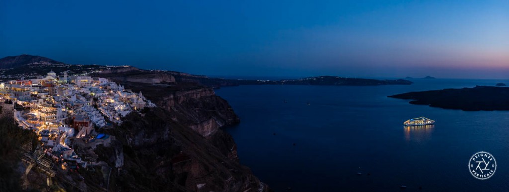 Panoramique sur le bateau de croisière qui passe la nuit au pied des falaises de Santorin