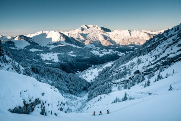 3 skieurs de randonnée font leur trace devant la Tournette qui s'illumine, France. Format paysage.