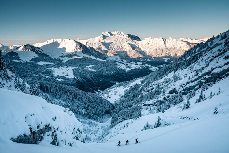 3 skieurs de randonnée font leur trace devant la Tournette qui s'illumine, France. Format paysage.